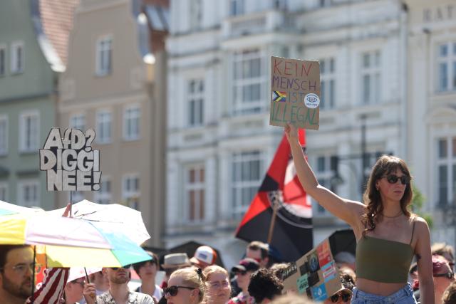 11 July 2026, Mecklenburg-Western Pomerania, Rostock: A participant in a counter-demonstration against the Alternative for Germany (AfD) rally, held under the slogan "Stop Left-Wing Violence!," holds up a sign at Neuer Markt that reads "No one is illegal". Photo: Danny Gohlke/dpa