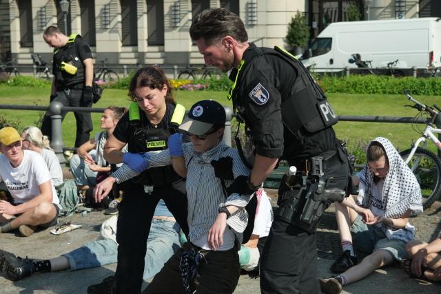 13 July 2026, Berlin: Police officers escort an activist away from the Brandenburg Gate during a protest against defence contractor Rheinmetall in Berlin. Photo: Sven Kaeuler/dpa