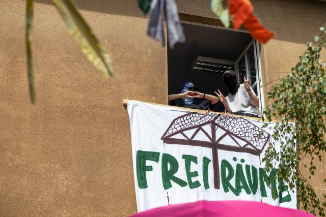 13 July 2026, Hesse, Giessen: Masked activists pose from a window of the Justus Liebig University building they have occupied. Photo: Christian Lademann/dpa