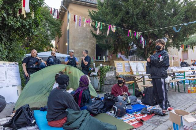 14 July 2026, Hesse, Giessen: Activists sit in tents and on blankets on the grounds of an occupied building at Justus Liebig University Giessen on Hein-Heckroth-Strasse, as police clear the premises after the occupation began on Saturday. Photo: Christian Lademann/dpa