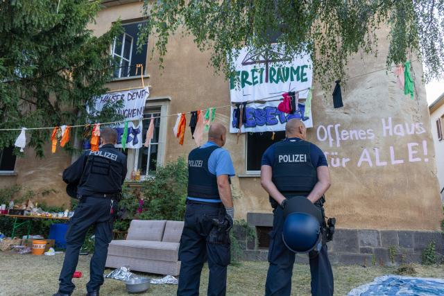 14 July 2026, Hesse, Giessen: Police officers stand in front of a building displaying banners with various messages during the clearance of a building at Justus Liebig University Giessen on Hein-Heckroth-Strasse. The building has been occupied by activists since Saturday. Photo: Christian Lademann/dpa