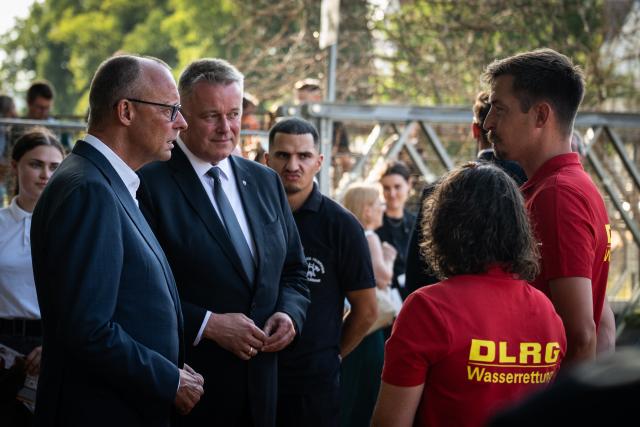 14 July 2026, Rhineland-Palatinate, Bad Neuenahr-Ahrweiler: German Chancellor Friedrich Merz (L) and Gordon Schnieder (2nd L), Minister-President of Rhineland-Palatinate, speak with members of the DLRG during a tour of the municipal construction site in the Kurpark, on the anniversary of the 2021 European floods. During the flood disaster in the summer of 2021, 136 people died in Rhineland-Palatinate, 135 of them in the Ahr Valley. Photo: Hannes P. Albert/dpa