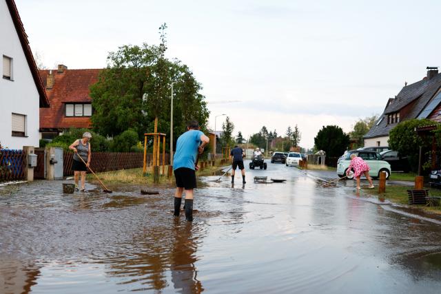 14 July 2026, Bavaria, Erlangen: Residents clear floodwater from a street after a thunderstorm in Erlangen. Photo: News5 / David Oßwald/NEWS5/dpa
