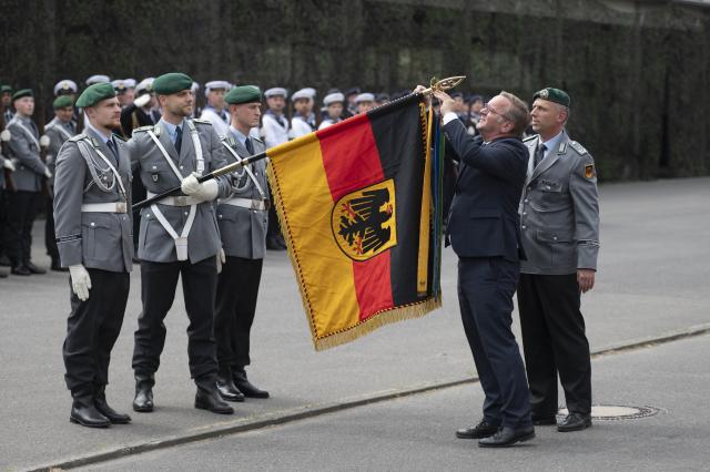 15 July 2026, Berlin: German Defense Minister Boris Pistorius attaches a ribbon to a military flag during a visit to the Guard Battalion at the Julius Leber Barracks. Photo: Christophe Gateau/dpa