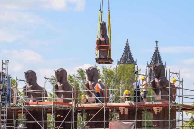 15 July 2026, Saxony-Anhalt, Magdeburg: A crane lifts a restored horse sculpture back onto the historic Horse Gate in Rotehorn Park, with Magdeburg Cathedral visible in the background. The installation completes the return of all six horse sculptures following extensive structural restorations to the gate's foundations and brick pillars. Photo: Klaus-Dietmar Gabbert/dpa