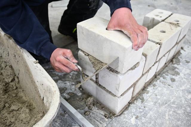 FILED - 14 March 2019, Baden-Wuerttemberg, Ravensburg: FILE PHOTO - An apprentice mason uses a trowel at a training center to remove excess mortar from the wall he built during a class. Photo: Felix Kästle/dpa