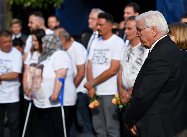 22 July 2026, Bavaria, Munich: Relatives of the victims and German President Frank-Walter Steinmeier (R) stand at the "Fuer Euch" (for you) memorial during the commemorative ceremony held by the City of Munich to mark the 10th anniversary of the attack on the Olympia Shopping Center. Photo: Sven Hoppe/dpa