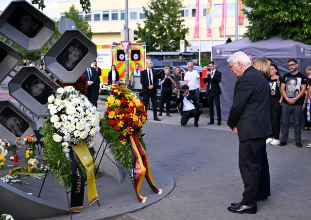 22 July 2026, Bavaria, Munich: Relatives of the victims and German President Frank-Walter Steinmeier (R) stand at the "Fuer Euch" (for you) memorial during the commemorative ceremony held by the City of Munich to mark the 10th anniversary of the attack on the Olympia Shopping Center. Photo: Sven Hoppe/dpa