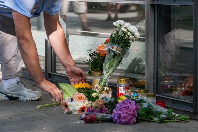 24 July 2026, Bavaria, Regensburg: A man lays flowers in front of the bank branch. Following the fatal knife attack at a bank in Regensburg, the criminal investigation department continues to try to uncover the circumstances surrounding the incident. Photo: Armin Weigel/dpa