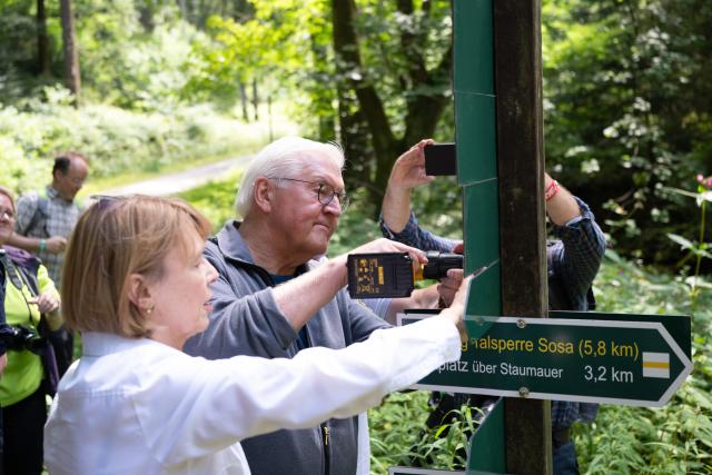 24 July 2026, Sachsen, Eibenstock: German President Frank-Walter Steinmeier, accompanied by his wife Elke Buedenbender, uses a drill to attach a sign to a trail marker on a hiking trail along the Sosa Dam. The visit marks the Eibenstock Charcoal-Burning Experience. Photo: Sebastian Kahnert/dpa