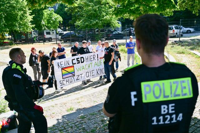 25 July 2026, Berlin: People stand behind a banner under the watchful eyes of police officers, chanting the slogan "We say 'No to CSD' - End the gender nonsense - There are only two genders: 'man and woman'" during a counter-demonstration against Christopher Street Day (CSD). Photo: Sebastian Gollnow/dpa