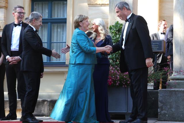 25 July 2026, Bavaria, Bayreuth: Former German Chancellor Angela Merkel is greeted by Bavarian Minister President Markus Soeder at the Festspielhaus, ahead of the opening of the Richard Wagner Festival. The Bayreuth Festival kicks off its 150th anniversary with Ludwig van Beethoven's Ninth Symphony. Photo: Karl-Josef Hildenbrand/dpa