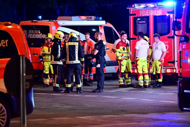 26 July 2026, Berlin: Police and fire department personnel stand next to emergency vehicles following the cancellation of Christopher Street Day (CSD). After a car struck and injured several people on the sidelines of Christopher Street Day in Berlin, police are searching for suspects. According to police, at least one person was killed in the incident on the outskirts of the event. Fourteen other people are currently being treated for injuries, said police spokesperson Nath. Photo: Fabian Sommer/dpa