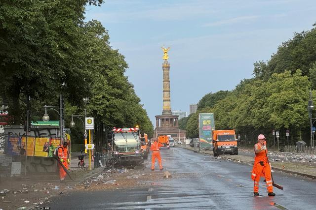 26 July 2026, Berlin: Employees of the Berlin City Cleaning Service (BSR) are cleaning up Straße des 17. Juni after Christopher Street Day (CSD)-the Victory Column can be seen in the background. CSD was cut short on Saturday evening after a car drove into a crowd on the outskirts of the large-scale event. Photo: Kathrin Deckart/dpa