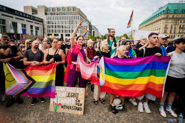 26 July 2026, Berlin: People hold flags during a demonstration in front of the Brandenburg Gate. Christopher Street Day in Berlin had been cut short the day before after a car plowed into a crowd on the outskirts of the large-scale event. Photo: Christoph Soeder/dpa