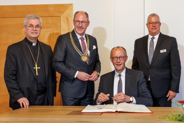 26 July 2026, North Rhine-Westphalia, Paderborn: German Chancellor Friedrich Merz (2nd R) signs the city's Golden Book as a guest of honor at the merchants' traditional Libori banquet, alongside Archbishop of Paderborn Udo Markus Bentz (L), mayor of Paderborn Stefan-Oliver Strate and Guild Master Johannes Beverungen (R). Photo: Friso Gentsch/dpa
