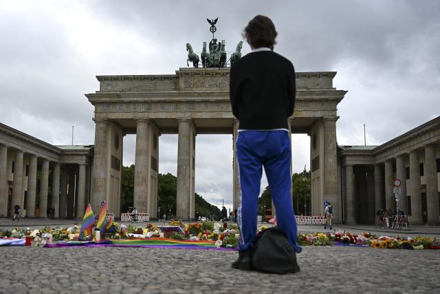 27 July 2026, Berlin: A person stands in front of the Brandenburg Gate, where flowers, candles, and personal messages have been left following the attack on the CSD. In the Tiergarten, on the sidelines of Christopher Street Day, a man drove a vehicle into a crowd. Photo: Markus Lenhardt/dpa