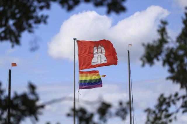 27 July 2026, Hamburg: A rainbow flag and a flag bearing the coat of arms of Hamburg hang from the flagpole of a boat rental shop on the Alster. Following the attack-believed to be Islamist-motivated-on revelers at Christopher Street Day (CSD) in Berlin, the Hamburg police plan to provide security for the queer community's large demonstration scheduled for this coming Saturday with additional personnel. Photo: Christian Charisius/dpa
