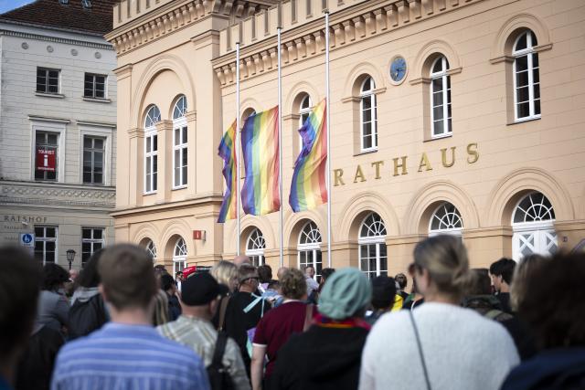 27 July 2026, Mecklenburg-Western Pomerania, Schwerin: Rainbow flags are flying at half-mast in front of Schwerin City Hall as people attend a vigil. Following the suspected Islamist terrorist attack on the sidelines of Christopher Street Day (CSD) in Berlin, the Schwerin CSD Association has called for a vigil in Mecklenburg-Western Pomerania's state capital. Photo: Philip Dulian/dpa