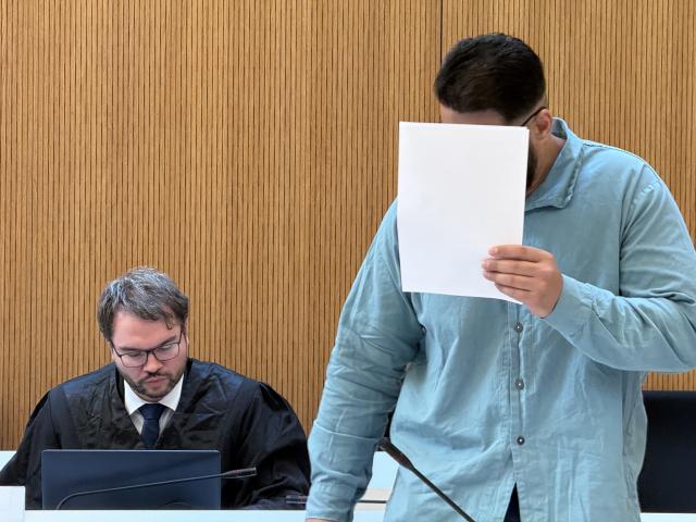 28 July 2026, Bavaria, Munich: The defendant, Farhad N, covers his face as he stands in the courtroom next to his attorney, Johann Bund. Farhad N. is charged with two counts of murder following a car attack on a demonstration in Munich on February 13, 2025. Photo: Elke Richter/dpa