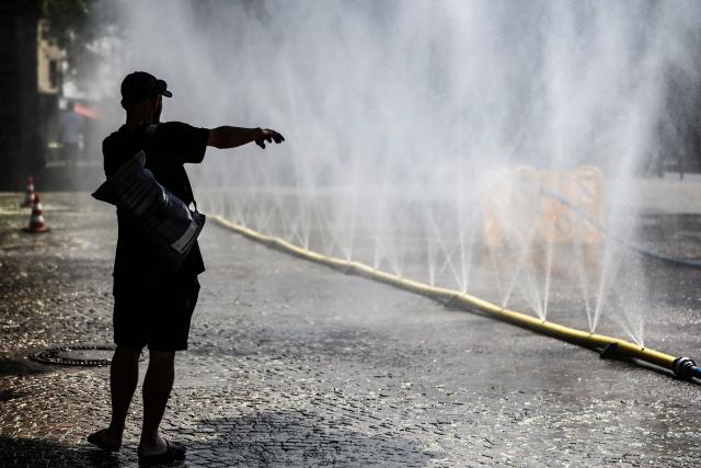 29 July 2026, North Rhine-Westphalia, Cologne: A man stands in front of a hose spraying a mist of water. The coming days are expected to remain hot in North Rhine-Westphalia, with temperatures reaching up to 36 degrees Celsius. Photo: Oliver Berg/dpa