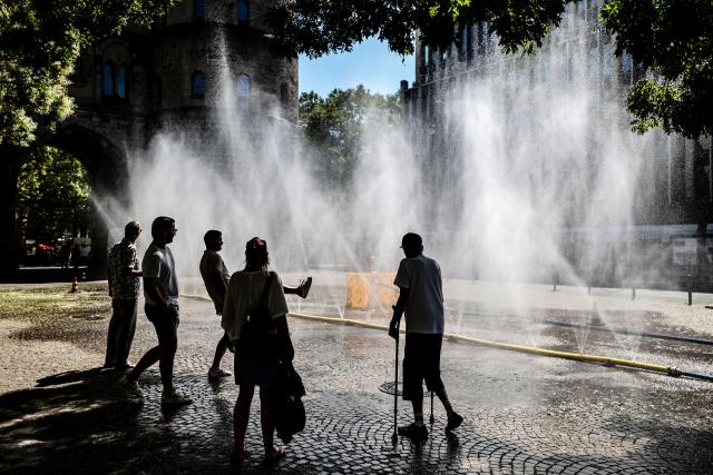 29 July 2026, North Rhine-Westphalia, Cologne: Passersby stand in front of a hose spraying a mist of water. The coming days are expected to remain hot in North Rhine-Westphalia, with temperatures reaching up to 36 degrees Celsius. Photo: Oliver Berg/dpa