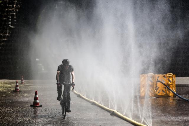 29 July 2026, North Rhine-Westphalia, Cologne: A man rides his bike past a hose spraying a mist of water. The coming days are expected to remain hot in North Rhine-Westphalia, with temperatures reaching up to 36 degrees Celsius. Photo: Oliver Berg/dpa