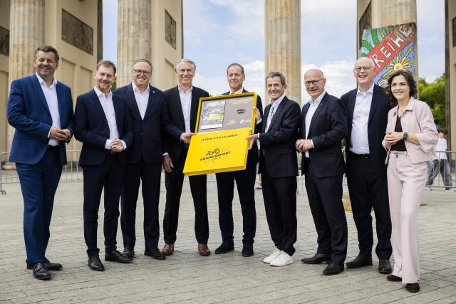 29 July 2026, Berlin: (L-R) Minister-President of Saxony-Anhalt Sven Schulze, Minister-President of Saxony Michael Kretschmer, Minister-President of Thuringia Mario Voigt, President of the German Cycling Federation Bernd Dankowski, Director of the Tour de France Christian Prudhomme, Managing Director of ASO Germany Yann Le Moenner, Governing Mayor of Berlin Kai Wegner, Rudolf Scharping and Minister of State and Federal Government Commissioner for Eastern Germany Elisabeth Kaiser stand in front of the Brandenburg Gate during a photo of marking the handover of the bid to host the start of the 2029 Tour de France in Central Germany to Tour Director Prudhomme. Photo: Christoph Soeder/dpa