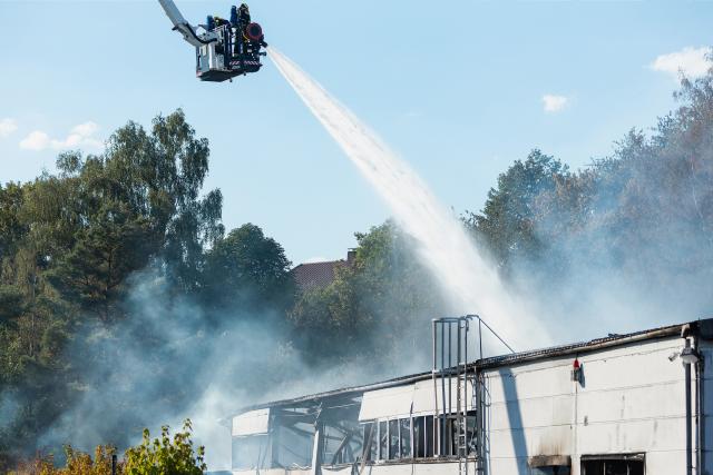 29 July 2026, Saarland, Neunkirchen: A firefighter conducts mop-up operations at an industrial building in the Wellesweiler district. Several people were injured in a major fire at a recycling facility for spray cans and similar pressurized containers. Photo: Laszlo Pinter/dpa