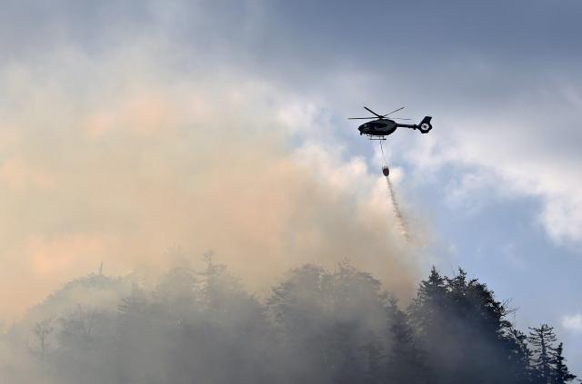 30 July 2026, Bavaria, Unterwössen: A helicopter is dropping water to fight a fire in the mountain forest of the Chiemgau Alps. Photo: Uwe Lein/dpa