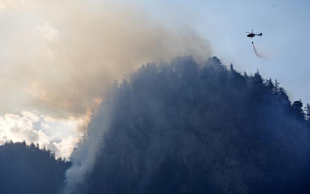 30 July 2026, Bavaria, Unterwössen: A helicopter is dropping water to fight a fire in the mountain forest of the Chiemgau Alps. Photo: Uwe Lein/dpa