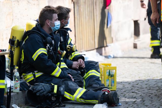 30 July 2026, Hesse, Lauterbach (Hessen): Firefighters rest during a mop-up operations, after a major blaze damaged several half-timbered houses. Initial estimates by the local fire department indicate that the fire in the central German state of Hesse caused at least five million euros in property. Photo: Florian Wiegand/dpa