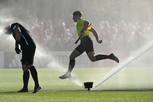 30 July 2026, Bavaria, Rottach-Egern: The linesman jumps over a sprinkler while Rottach-Egern goalkeeper Killian Zimmer cools off during the Friendly soccer match between FC Rottach-Egern and FC Bayern Munich. Photo: Peter Kneffel/dpa - WICHTIGER HINWEIS: Gemäß den Vorgaben der DFL Deutsche Fußball Liga bzw. des DFB Deutscher Fußball-Bund ist es untersagt, in dem Stadion und/oder vom Spiel angefertigte Fotoaufnahmen in Form von Sequenzbildern und/oder videoähnlichen Fotostrecken zu verwerten bzw. verwerten zu lassen.