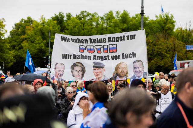 01 August 2026, Berlin: Participants in a demonstration organized by the "We Are Many" coalition are protesting in front of the Brandenburg Gate under the slogan "Off to Berlin for peace, freedom, fundamental rights, and a genuine reckoning with the coronavirus crisis." A banner featuring, among other things, a photo of the German chancellor reads, "We're not afraid of Putin; we're afraid of you." Photo: Christoph Soeder/dpa