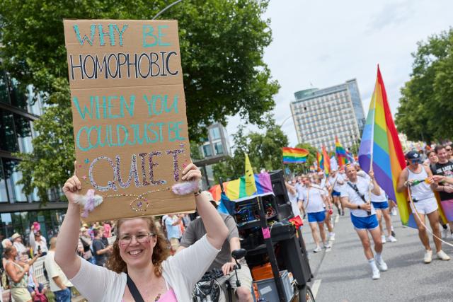 01 August 2026, Hamburg: A participant holds up a banner reading "Why be homophobic when you could just be quiet" during Hamburg Pride 2026, the Christopher Street Day (CSD) parade on Steindamm. Photo: Georg Wendt/dpa
