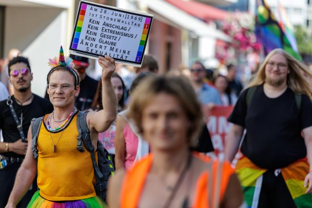 01 August 2026, North Rhine-Westphalia, Moers: A participant in the Christopher Street Day (CSD) Pride Parade holds a sign that reads, "No attack, no extremism, no law, no faith can change my sexuality". Photo: David Ebener/dpa