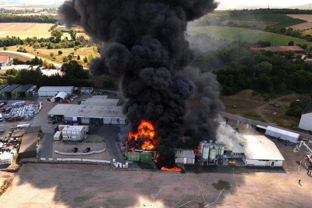 02 August 2026, Rhineland-Palatinate, Sprendlingen: Flames and thick smoke billow from the buildings of a plastics factory in Sprendlingen after a major fire broke out. Several adjacent residential buildings have been evacuated, and emergency responders are assisting several residents, according to the Mainz-Bingen district. The railroad line near Sprendlingen has been closed as a precaution. Photo: Christian Schulz/Kamerateam Hosser/dpa