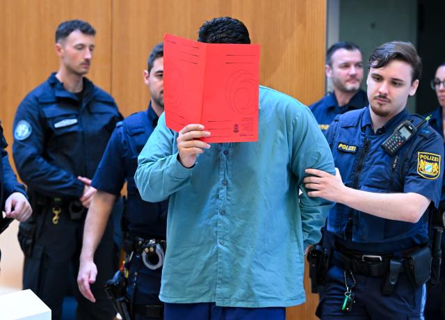 06 August 2026, Bavaria, Munich: The defendant Farhad N. (R) is escorted into the courtroom by police officers at the start of his trial. The 25-year-old Afghan national faces two counts of murder and multiple counts of attempted murder after allegedly ramming a car into a trade union demonstration in central Munich on February 13, 2025. Photo: Sven Hoppe/dpa