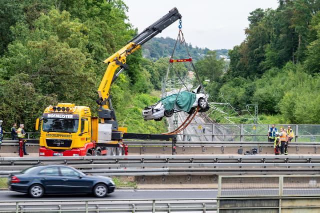 06 August 2026, Bavaria, Nittendorf: Emergency responders recover the wreckage of a car from a railway line running beneath the A3 motorway. Three people were killed after their vehicle veered off the highway and plunged down an embankment onto the busy Nuremberg-Regensburg train tracks. Photo: Armin Weigel/dpa