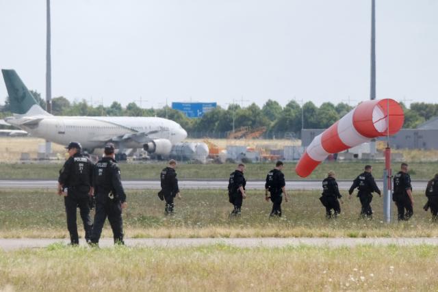 07 August 2026, Saxony, Schkeuditz: Police officers walk across a field on the grounds of Leipzig/Halle Airport. The investigation into the discovery of a drone carrying an explosive device is ongoing. Numerous police officers are searching the area on foot near the northern runway. Photo: Sebastian Willnow/dpa
