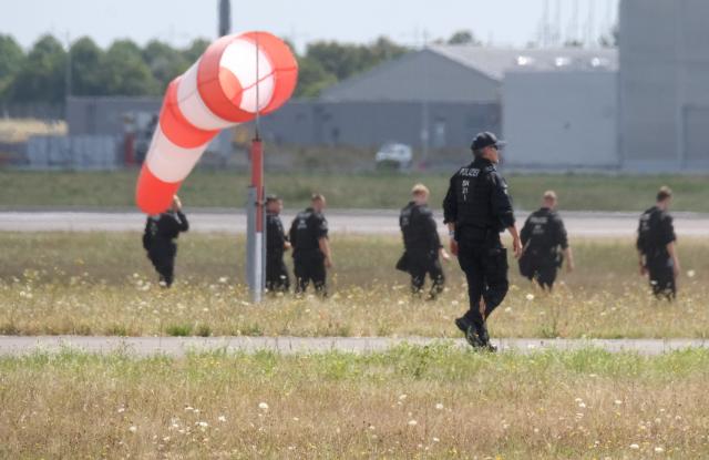 07 August 2026, Saxony, Schkeuditz: Police officers walk across a field on the grounds of Leipzig/Halle Airport. The investigation into the discovery of a drone carrying an explosive device is ongoing. Numerous police officers are searching the area on foot near the northern runway. Photo: Sebastian Willnow/dpa