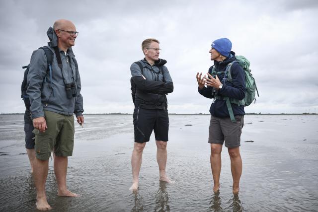 07 August 2026, Schleswig-Holstein, Hallig Oland: Schleswig-Holstein's Minister President Daniel Guenther (C), Tobias Goldschmidt (L), Schleswig-Holstein's Minister of the Environment, and Jennifer Buchner of the National Park Administration, talk during a mudflat hike organized by the National Park Administration from Dagebuell to the Hallig Oland. Photo: Christian Charisius/dpa