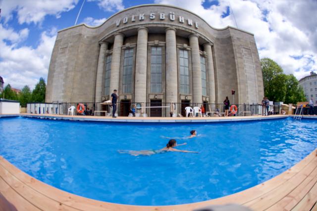 07 August 2026, Berlin: Lifeguards Helena and Donate swim in the public pool in front of the Volksbuehne theatre at Rosa-Luxemburg-Platz. The new artistic director, Lilienthal, is opening the season with Volksbad. The pool is scheduled to remain open through October. Photo: Soeren Stache/dpa
