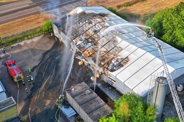 09 August 2026, Rhineland-Palatinate, Bad Sobernheim: An aerial view taken with a drone shows firefighters are extinguishing a fire in a warehouse storing plastic from a work basket attached to a turntable ladder. The damage caused by the fire at the former German Armed Forces airfield is estimated at around 600,000 euros. Photo: Sebastian Schmitt/dpa