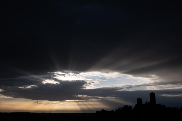 09 August 2026, Hesse, Muenzenberg: Rays of sunlight pierce through the rain clouds behind the Muenzenberg castle ruins. Photo: Florian Wiegand/dpa