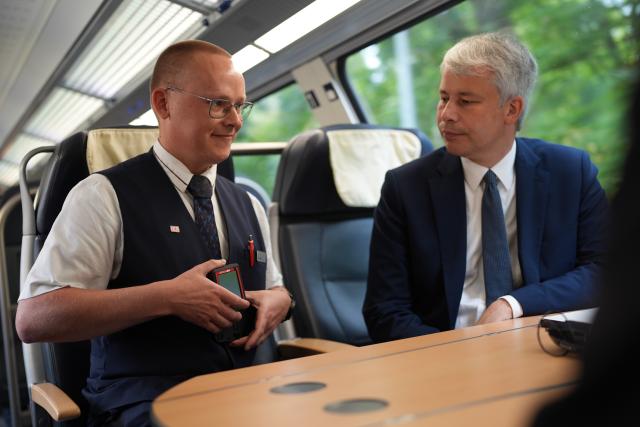 10 August 2026, Schleswig-Holstein, Pinneberg: Steffen Bilger (R), German Minister of Transportation, talks with train attendant Nils Koester-a customer service representative for commuter rail-about safety on the train while riding the RE 7 from Pinneberg to Kiel, and has him explain how a body camera works.
During his summer tour, Transportation Minister Bilger is visiting various projects in northern Germany. Photo: Marcus Brandt/dpa