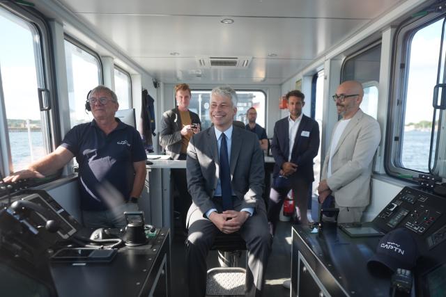 11 August 2026, Schleswig-Holstein, Kiel: German Transport Minister Steffen Bilger (C) sits in the captain's chair during a trip aboard the autonomous ferry "MS Wavelab" on the Kiel Fjord. The 20-metre-long, eight-metre-wide catamaran is being used to test autonomous and semi-automated passenger shipping on the Kiel Fjord. Photo: Marcus Brandt/dpa