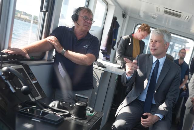 11 August 2026, Schleswig-Holstein, Kiel: German Transport Minister Steffen Bilger (R) sits in the captain's chair during a trip aboard the autonomous ferry "MS Wavelab" on the Kiel Fjord. The 20-metre-long, eight-metre-wide catamaran is being used to test autonomous and semi-automated passenger shipping on the Kiel Fjord. Photo: Marcus Brandt/dpa