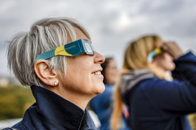 FILED - 24 October 2022, Hamburg: FILE PHOTO - A visitor to the Hamburg Planetarium watches a partial solar eclipse from the observation deck while wearing protective glasses. Photo: Axel Heimken/dpa