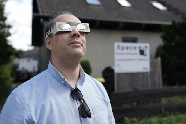 PRODUCTION - 11 August 2026, Berlin: Christopher Foerster, who runs the Space Instruments telescope shop in Berlin-Lichtenrade, demonstrates how to wear solar eclipse glasses properly. He says he sold hundreds of pairs last week and another 300 on the day before the event. Experts warn against looking directly at the sun without certified solar viewing glasses. Photo: Manuel Genolet/dpa